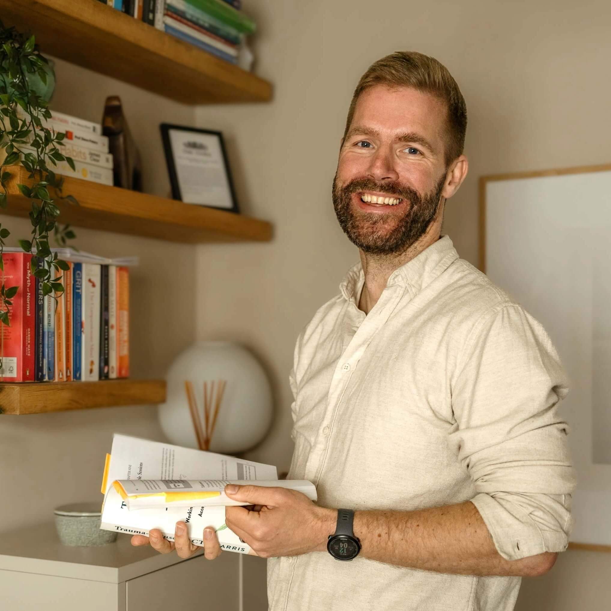Nick standing in his office holding a book about neurodiverse coaching.